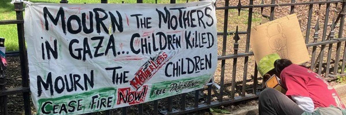 A banner on a fence reads, "Mourn the mothers in Gaza... children killed. Mourn the children."