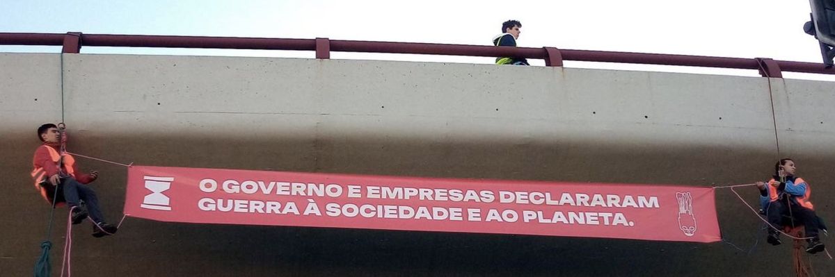 A banner reading, "Government and businesses declare war on society and the planet," in Portuguese.
