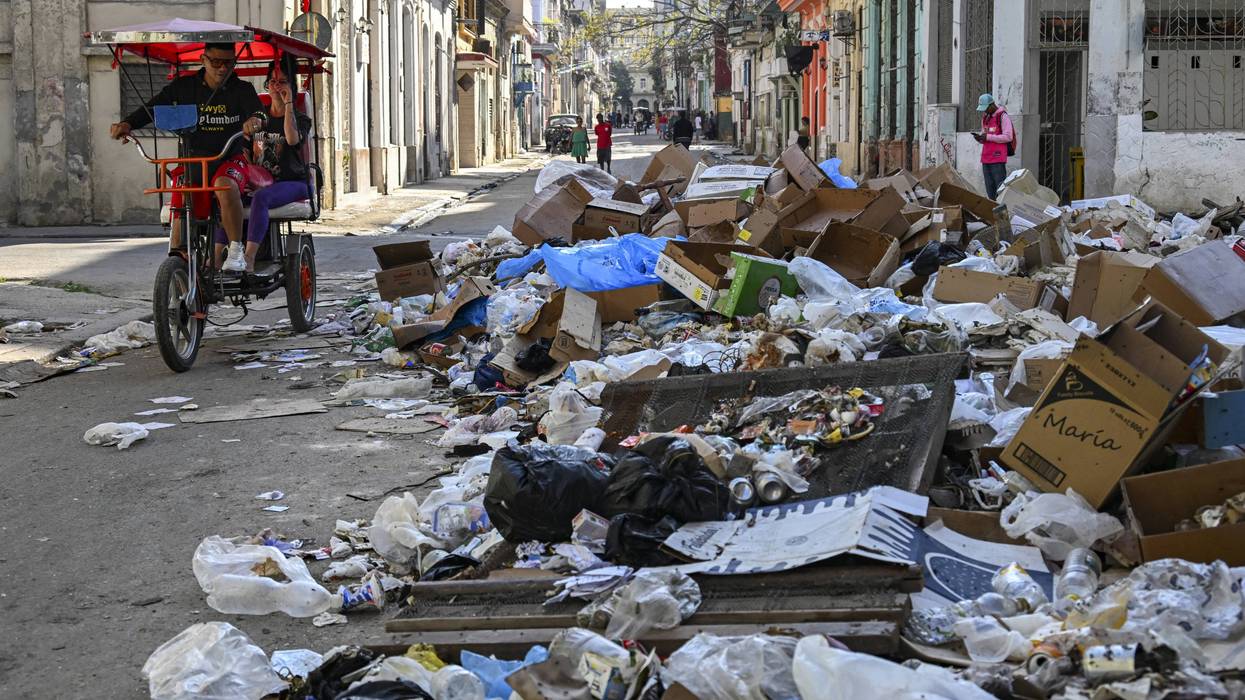 A bicitaxi rides past garbage piled up on a street in Havana