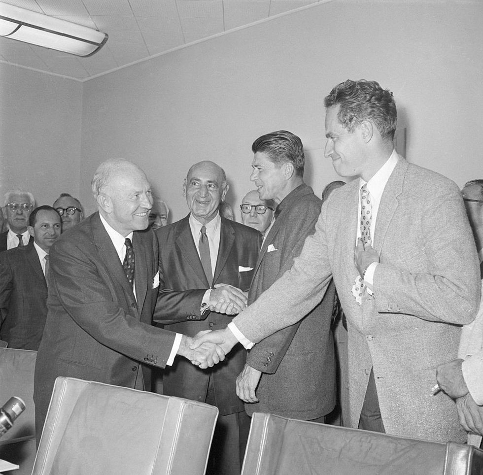A black-and-white image of Charlton Heston and Ronald Reagan shaking hands with Hollywood studio leaders in 1960.