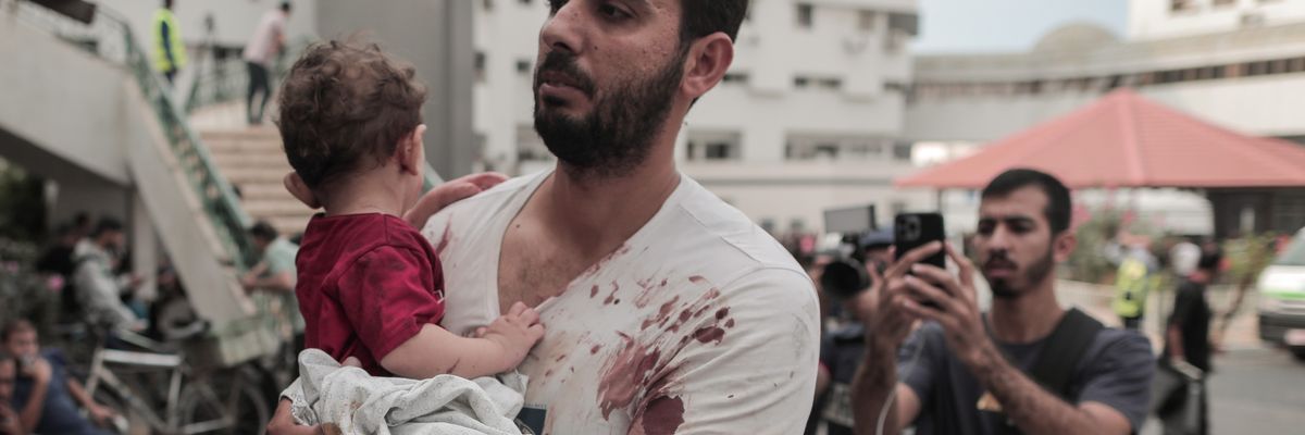 A bloodied Palestinian man and his baby arrive at Gaza hospital
