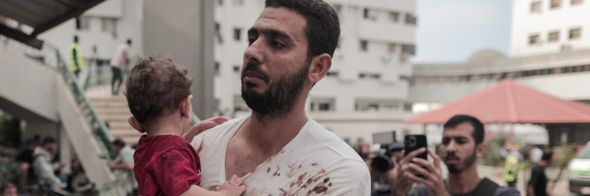 A bloodied Palestinian man and his baby arrive at Gaza hospital