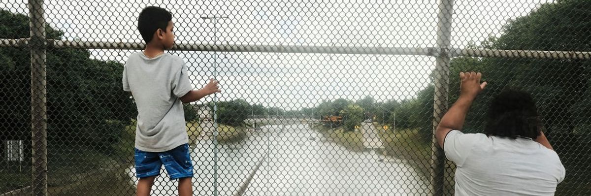 A boy and adult look through a chain-link fence at a flooded highway in Detroit.