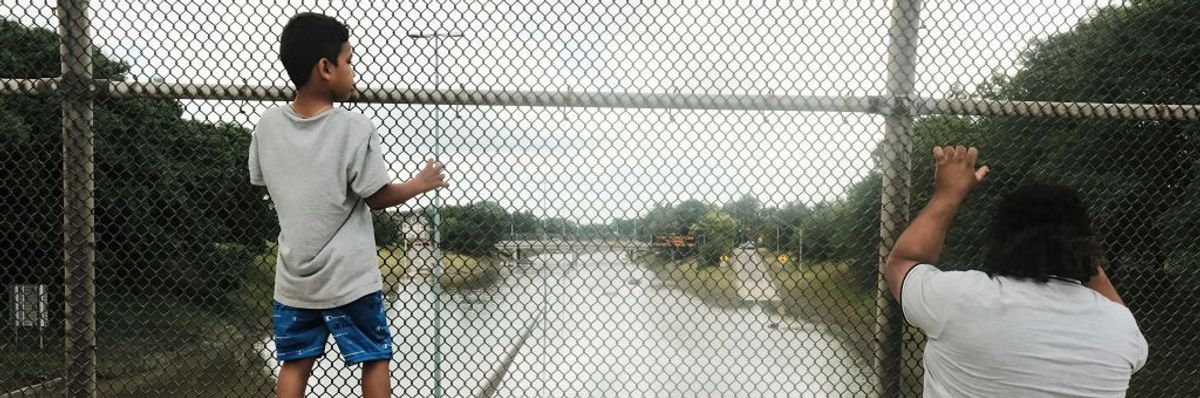 A boy and adult look through a chain-link fence at a flooded highway in Detroit. 