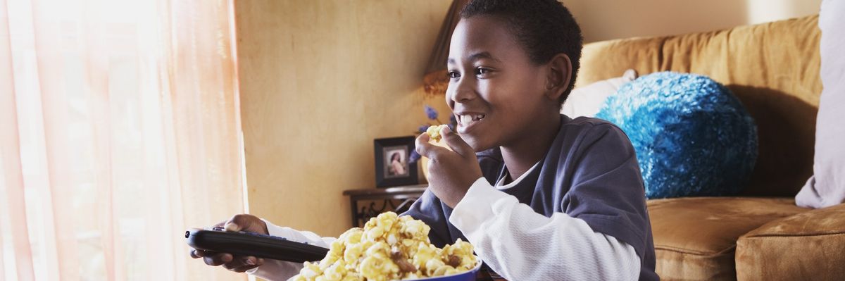 a boy eats popcorn while watching tv