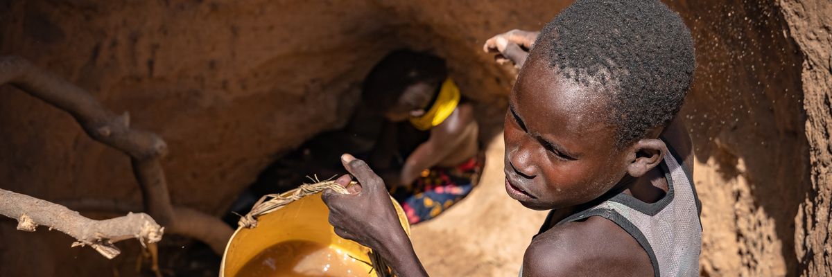A boy holds a pail with brown water from a well