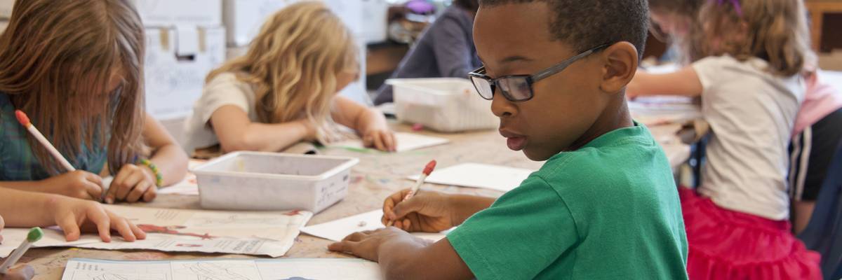 A boy in a green shirt sits at a public school desk