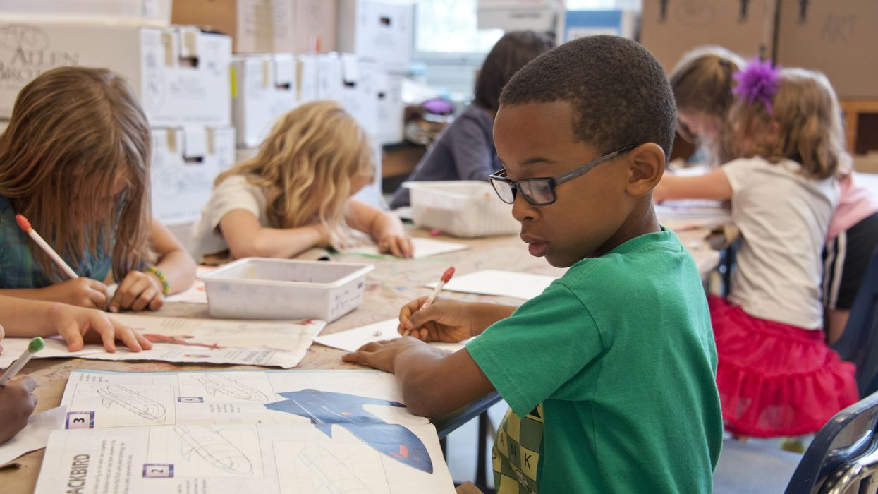 A boy in a green shirt sits at a public school desk