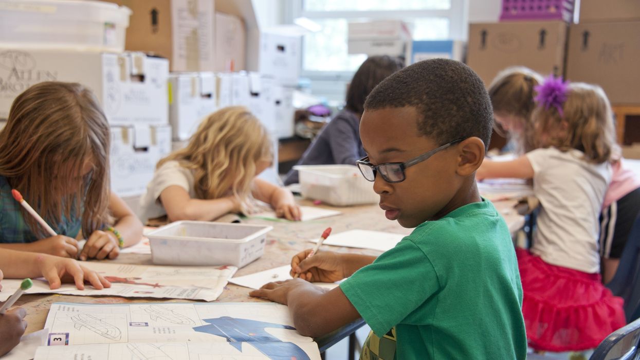 A boy in a green shirt sits at a public school desk