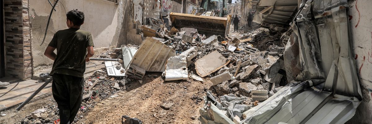 A boy walks before a bulldozer clearing rubble