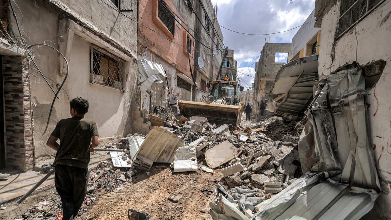 A boy walks before a bulldozer clearing rubble