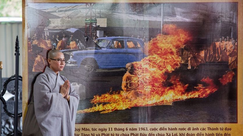 A Buddhist monk stands next to a banner showing Thick Quang Duc's 1963 self-immolation. 