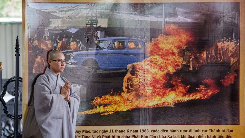 A Buddhist monk stands next to a banner showing Thick Quang Duc's 1963 self-immolation.