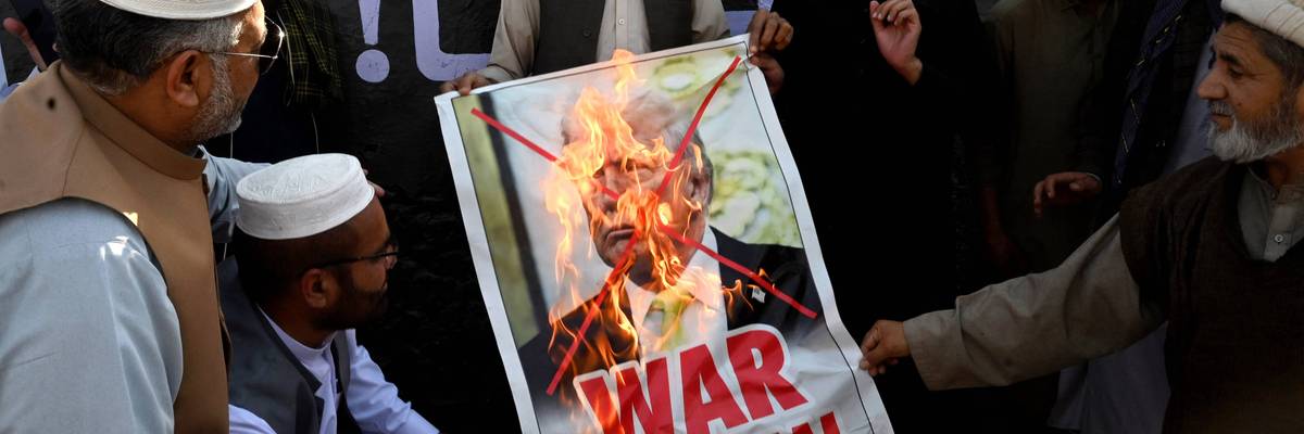 A burning photo of Trump says, "War criminal."