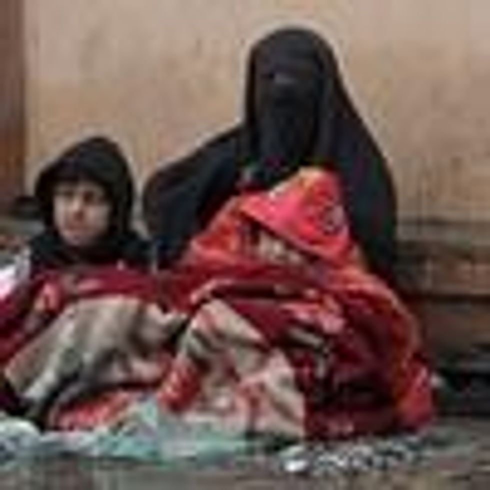A burqa-clad Afghan woman sits next to a boundary wall with her children as she seeks alms from people passing by along a road in Kabul on January 8, 2022