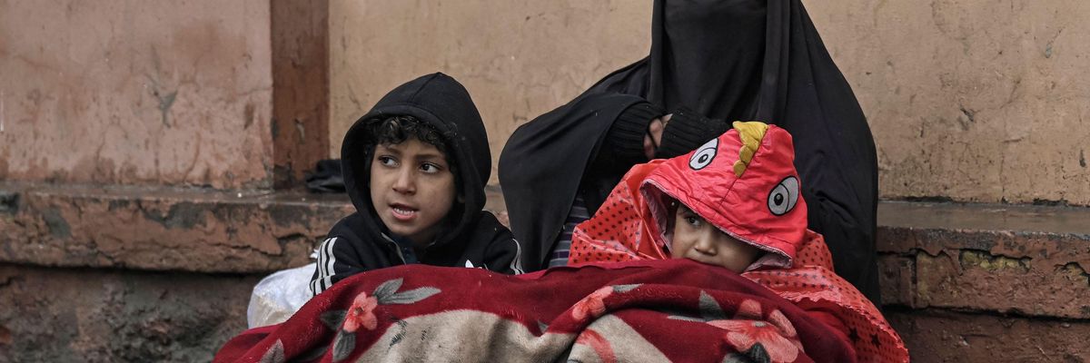 A burqa-clad Afghan woman sits next to a boundary wall with her children as she seeks alms from people passing by along a road in Kabul on January 8, 2022