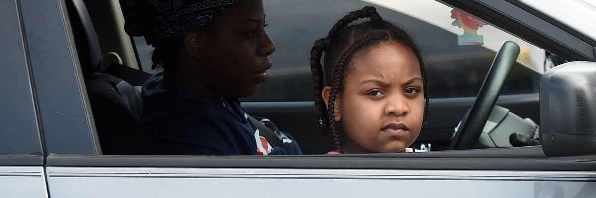 A child and her mother wait in their car at a food distribution site at Lake-Sumter State College