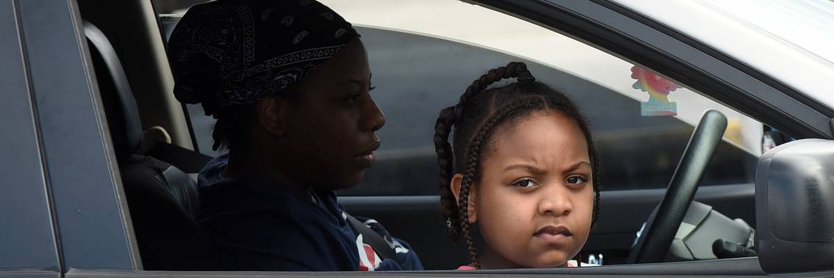 A child and her mother wait in their car at a food