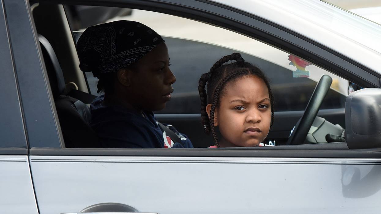 A child and her mother wait in their car at a food