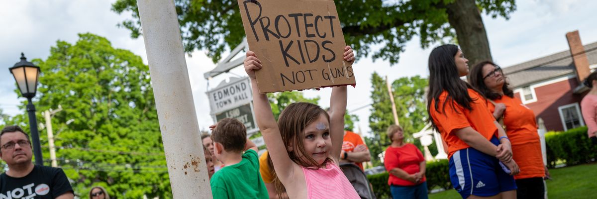 A child holds up a sign that reads "Protect Kids, Not Guns" 