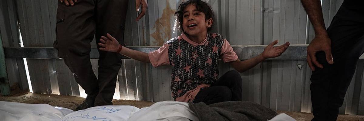 A child holds up their hands over bodies killed in Gaza.