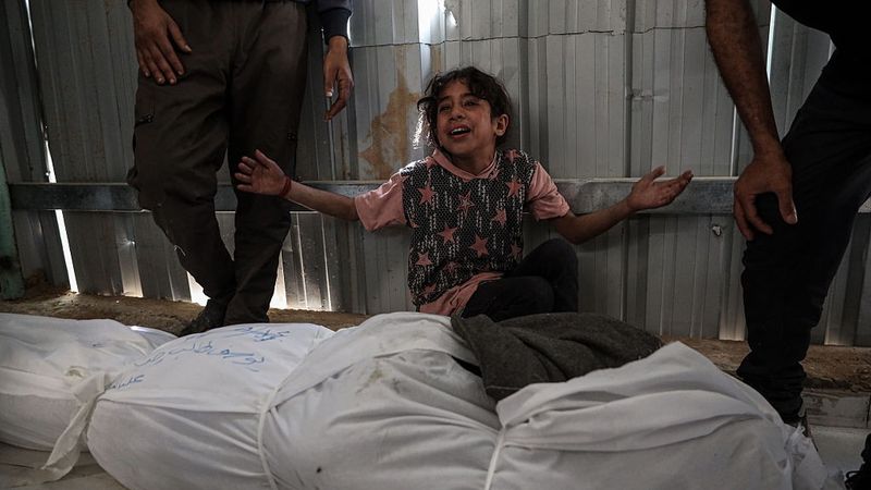 A child holds up their hands over bodies killed in Gaza.