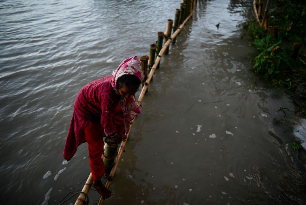 A child in red climbs over a bamboo barrier in a flooded river.