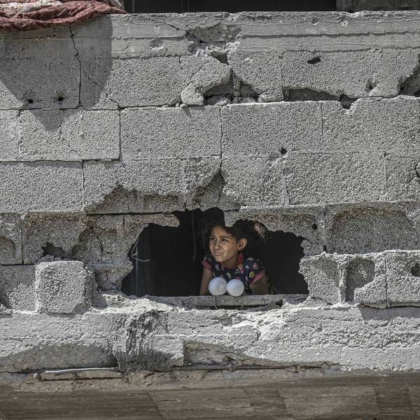A child peers through a hole in a damaged concrete wall