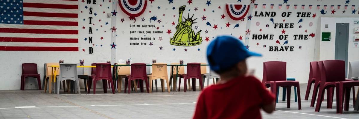 A child plays while detained in an ICE facility with "land of the free, home of the brave" written on a wall