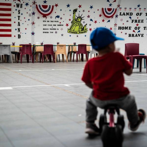 A child plays while detained in an ICE facility with "land of the free, home of the brave" written on a wall