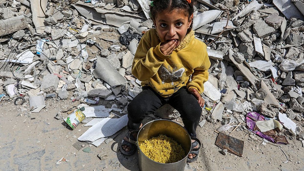 A child stands in front of rubble in Gaza with food aid.