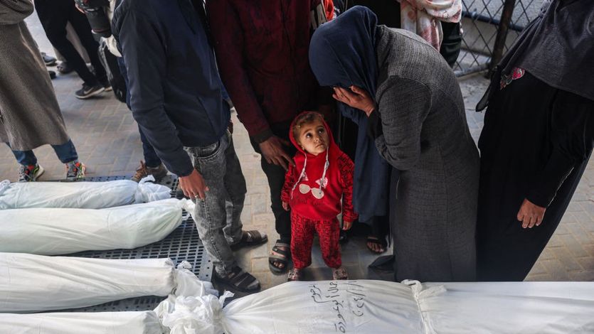 A child watches as a mourner cries over bodies