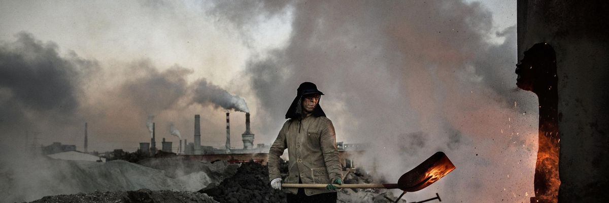 A Chinese laborer loads coal into a furnace as smoke and steam rises from an unauthorized steel factory