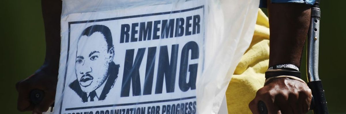 A closeup of a sign worn by a demonstrator reading, "Remember King."