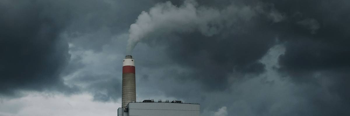 A coal power plant emits smoke against a cloudy sky.