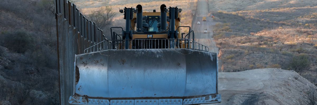A construction vehicle drives along the border wall
