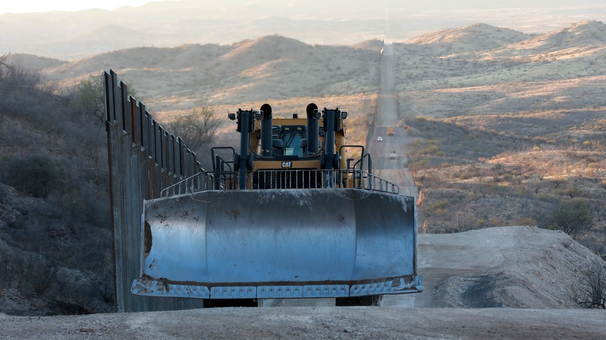 A construction vehicle drives along the border wall 