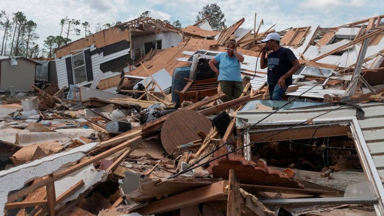 A couple stands in the ruins of their mobile home after a hurricane.