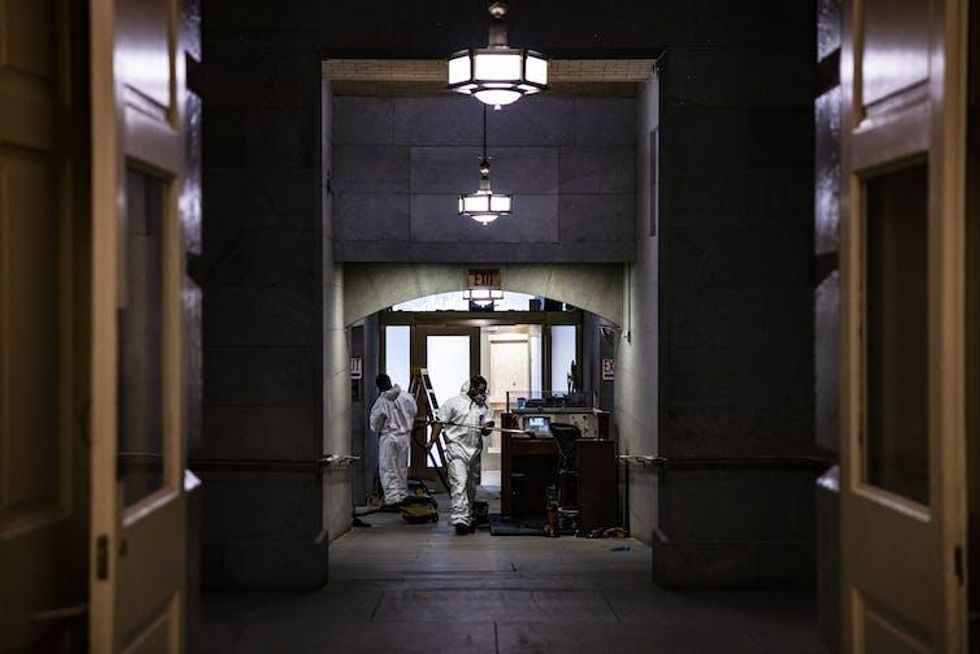 A dark hallway in the US Capitol building, with workers in white jumpsuits cleaning up damage.