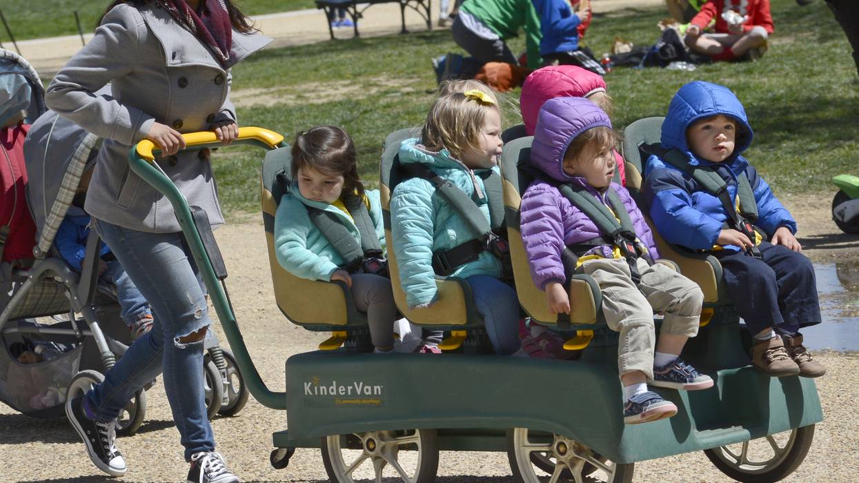A daycare employee pushes children in a cart.