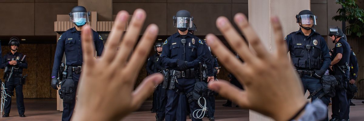 A demonstrater raises her hands in front of a line of police.
