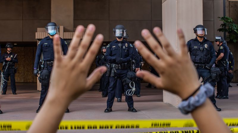 A demonstrater raises her hands in front of a line of police.