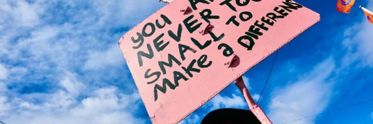 A demonstrator holds a sign reading, "You are never too small to make a difference."