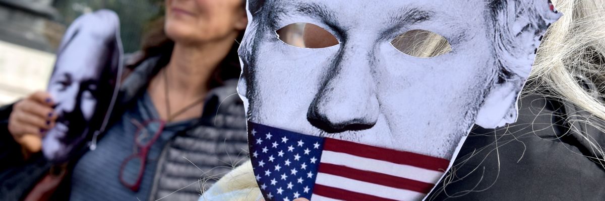 A demonstrator holds up a mask of Julian Assange being muzzled by the U.S. flag.