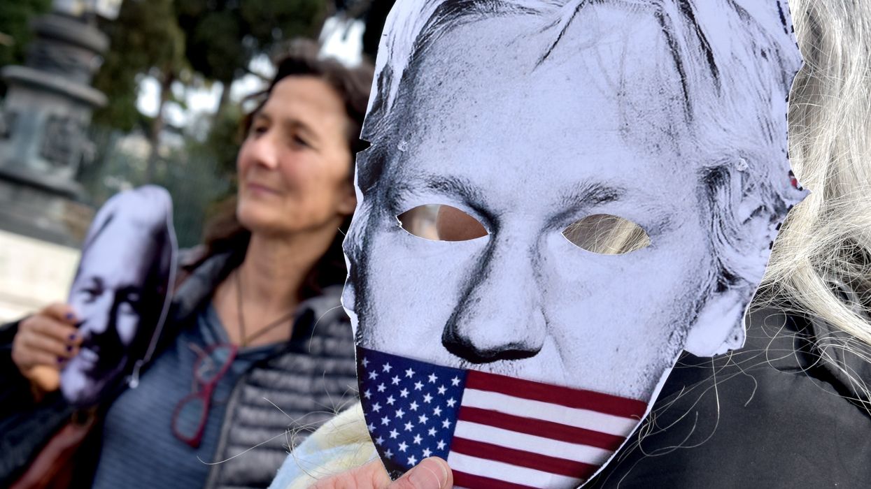 A demonstrator holds up a mask of Julian Assange being muzzled by the U.S. flag.