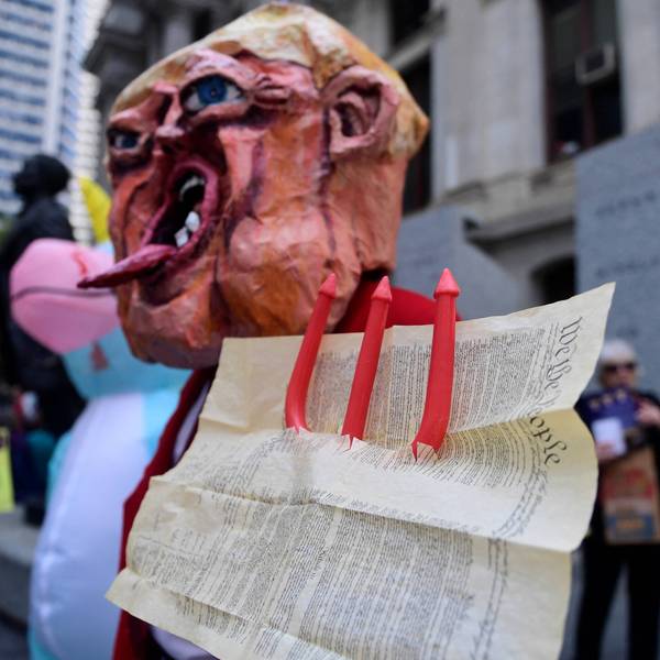 A distorted mask of Trump taking a pitchfork to the Constitution.