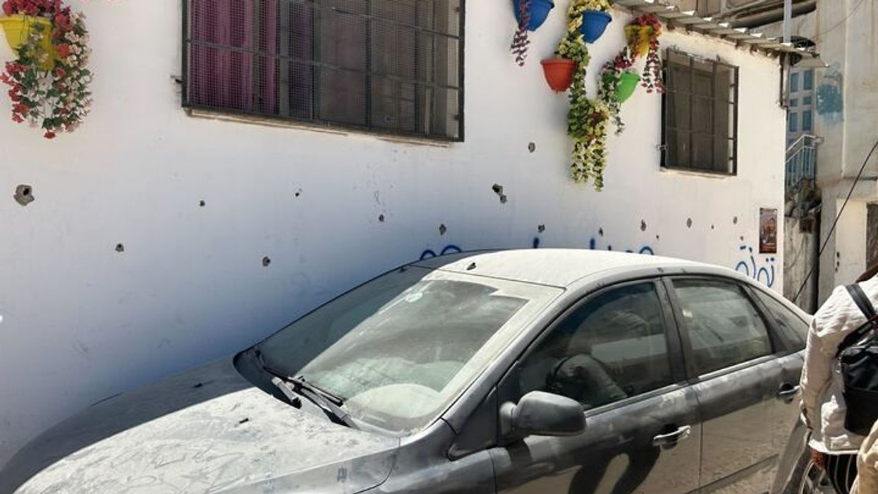A dusty car against a white wall with bullet holes.