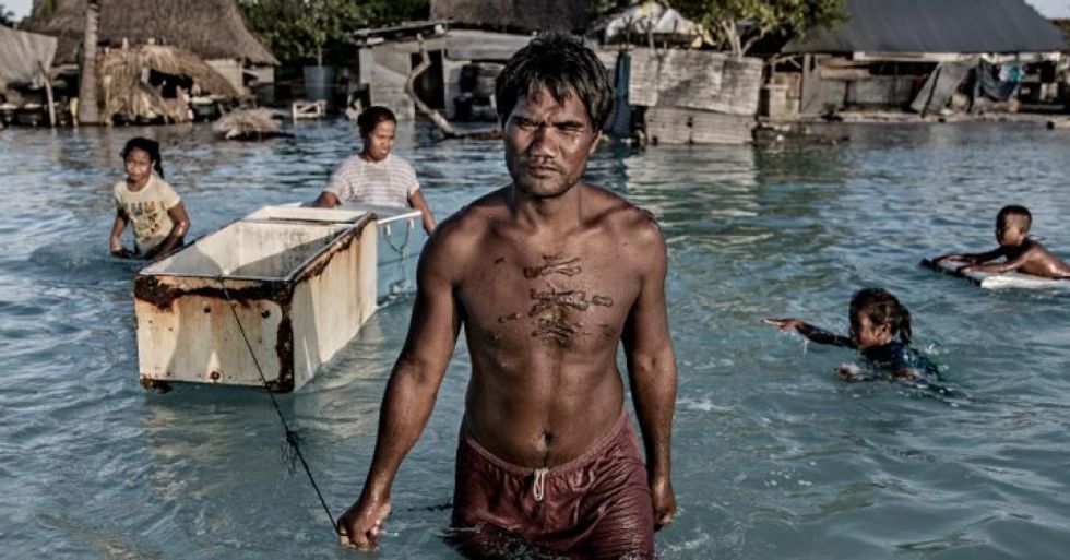 A family wading through the salty sea water that flooded their village in Eita, Kiribati, on September 30, 2015. They float an old refrigerator after themselves as they collect seabed-stones to build a stone wall to block out the floods. (Photo: Jonas Gratzer/LightRocket via Getty Images)