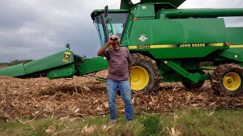 A farmer stands in front of a tractor.