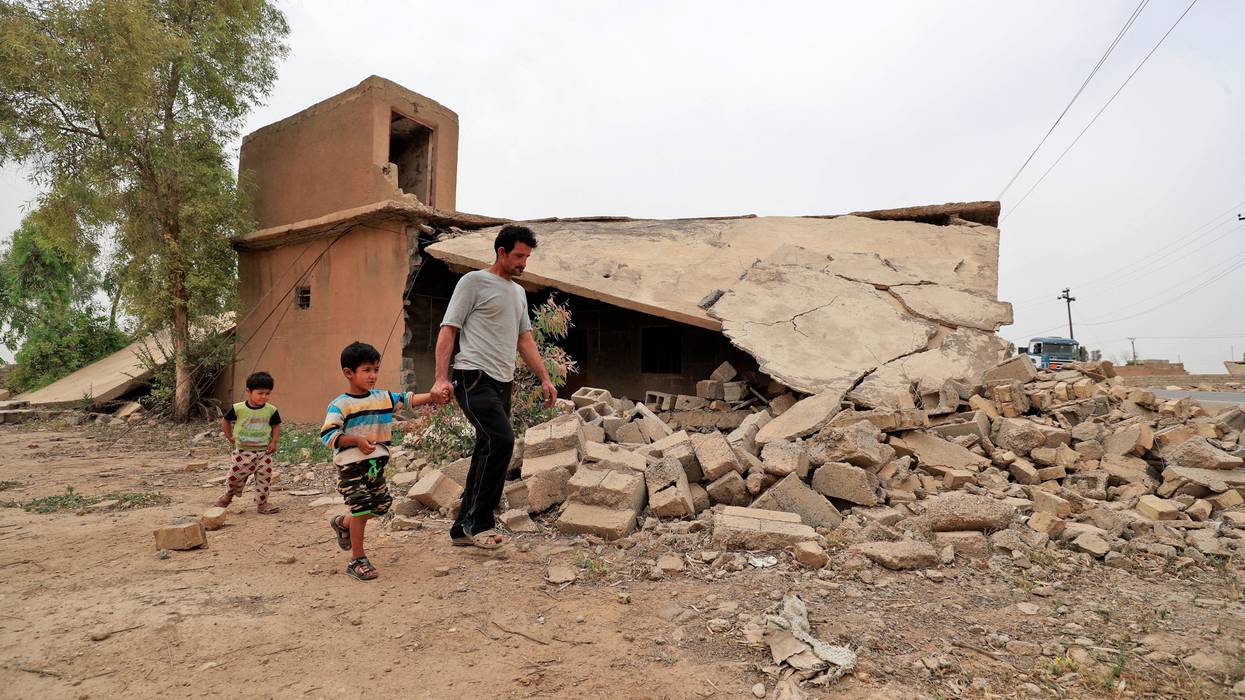 A father and children walk past a destroyed home in Iraq.
